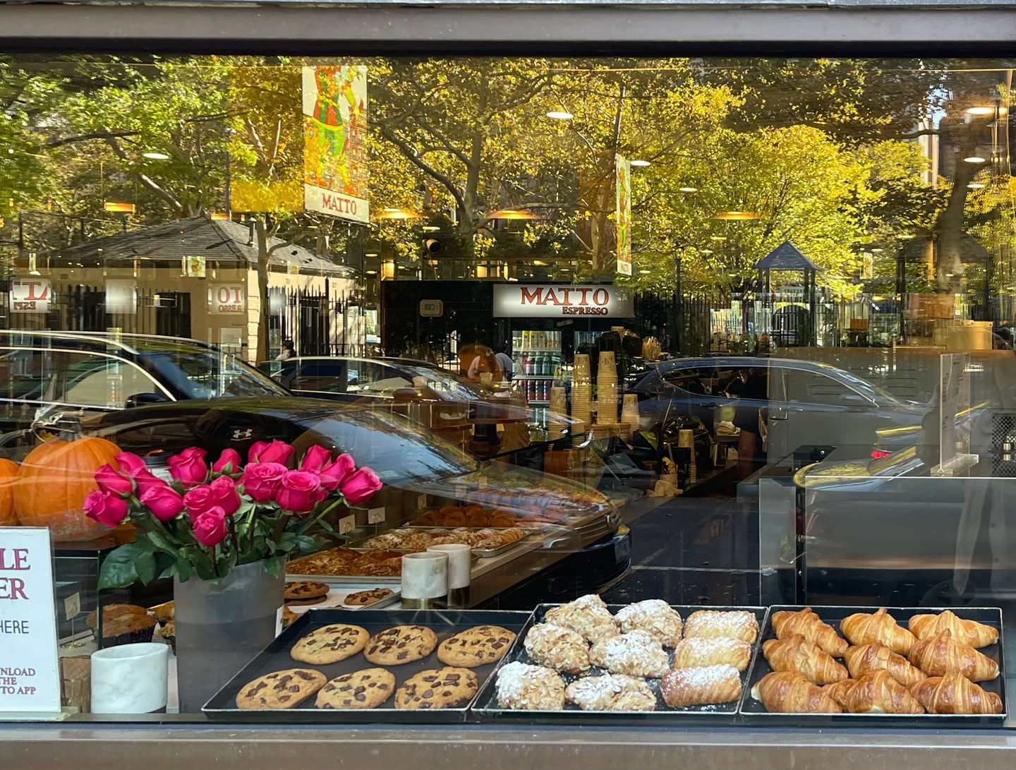 Cookies and croissants in a Matto window with flowers and a reflection of the city street